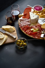 Antipasti board with cheese and meat snacks with red wine and baguette on board on black table