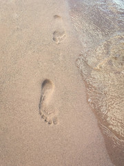 Two footprints in the sand along the waters edge