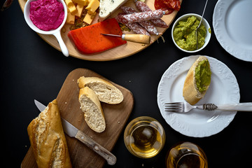 Antipasti board with cheese and meat snacks with white wine and baguette on board on black table
