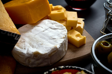 Close up on different kinds of cheese on wooden board on black table