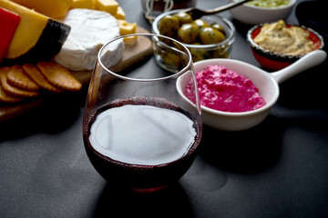 Antipasti board with different cheese and meat snacks with red wine on wooden board on black table