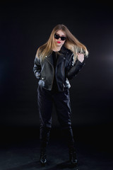 young girl in a black leather jacket and sunglasses on a dark background standing