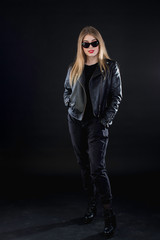 young girl in a black leather jacket and sunglasses on a dark background standing