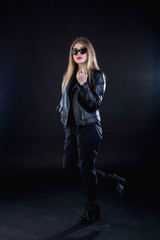 young girl in a black leather jacket and sunglasses on a dark background standing