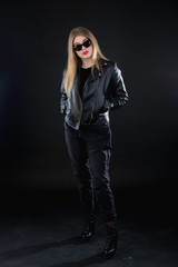 young girl in a black leather jacket and sunglasses on a dark background standing