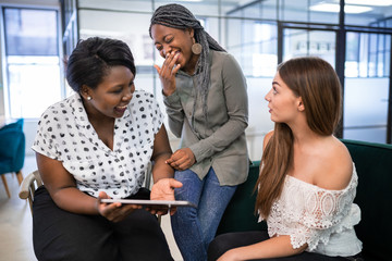 All woman mixed race group sitting, talking and laughing in a co-working space