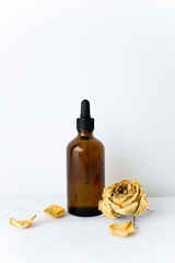Skincare product glass brown serum dropper bottle mockup sample styling with dried yellow roses on white fabric texture table top background with empty copy space. Product studio styling shot.