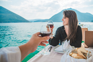 woman with man drinking wine in restaurant at seaside with beautiful view of bay and mountains