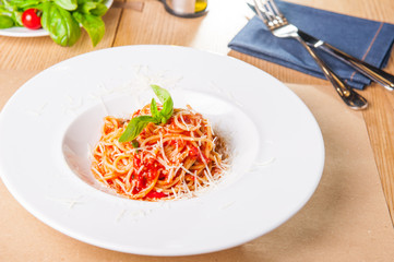 Fresh, cooked Italian spaghetti, pasta with marinara or tomato sauce decorated with basil on the white plate served on the wooden table with catlery. Selective focus, copy space.