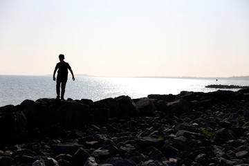 silhouette of teenage boy playing on the rocks at the beach