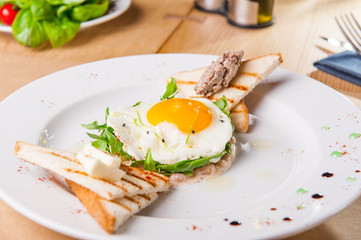 Close up Breakfast with fried eggs, toasts and meat pate on white plate on the served wooden table. Selective focus, copy space.