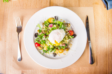 Top view Green Vegetable Salad with tuna and Poached Egg on the white plate on the wooden served table. Selective focus, copy space.