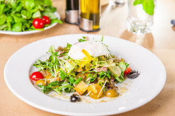 Close up Green Vegetable Salad with tuna and Poached Egg on the white plate on the wooden served table. Selective focus, copy space.