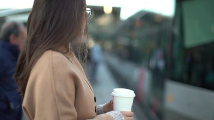 Slow motion profile european attractive female entrepreneur holding take-away morning coffee heading work waiting train station platform, commute home, living lively city, standing relaxed casually - Powered by Adobe