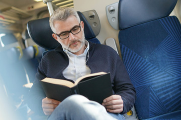 Mature man traveling by train, reading book