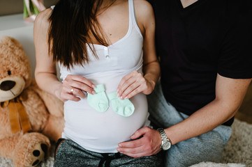 Cropped image of husband holding belly of his pregnant wife, socks for baby in hands. Pregnant...