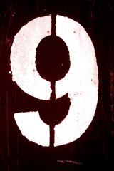 Number 9 in stencil on metal wall in red tone.