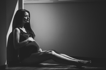 Waiting baby. Pregnant woman sitting near window and hands embraces a round belly, stomach. close-up. nine months. Baby Shower. Motherhood concept. Black and white photo.
