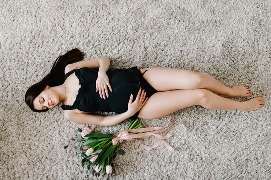 Pregnant happy sexy woman resting and lying on floor or bed, touching her belly holding a bouquet of flowers, hugging tummy at home. Motherhood concept. Pregnancy, expectation. flat lay. top view.