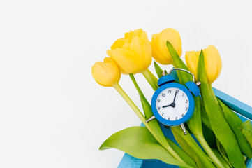Womans holiday yellow Spring tulips with an alarm clock and blue wooden cart box isolated on white background.Several objects Top horizontal view copyspace
