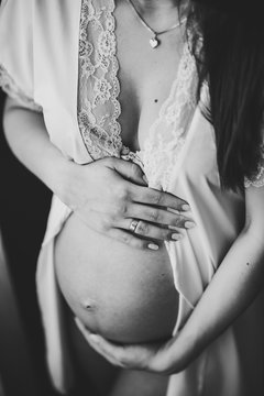 Pregnant Woman hold hands round stomach, girl embraces a round belly near the window at home. Maternity concept. Close up. nine months. Baby Shower. top front view. Black and white photo.
