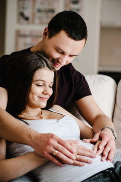 Image of husband holding belly of his pregnant wife making symbol heart hands. Pregnant woman and loving handsome man hugging tummy at home. Loving Couple. Parenthood concept. Baby Shower.