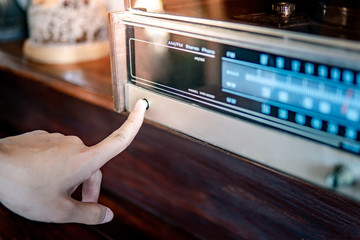 Male hand turning on retro radio by pressing power button. Listen to music or news with old classic radio receiver. Vintage lifestyle