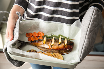 Woman holding baking dish with tasty mackerel fish and vegetables, closeup