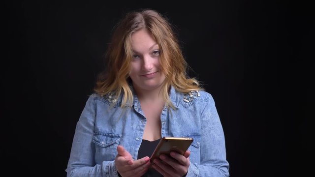 Closeup portrait of adult caucasian blonde female typing on the phone looking at camera and laughing happily