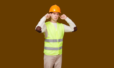 The young man in a construction helmet, a vest closed ears hands not to hear noise