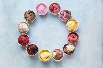 Different cups of ice cream flavors set in circle shape on rustic background with copy space, top view