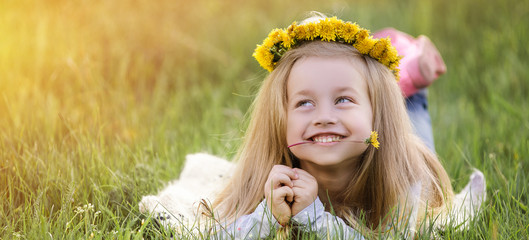 A girl in a wreath of dandelions lying on the grass. Spring concept