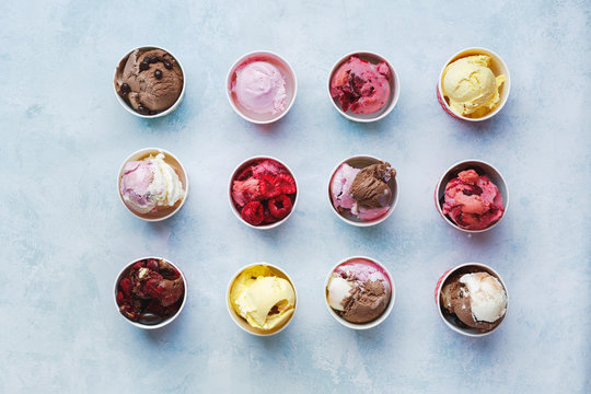 Scoops of fruits and chocolate ice cream in cups on rustic background, top view