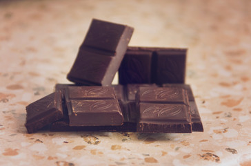 Tiles and slices of dark delicious chocolate on the marble countertop.