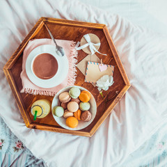 Breakfast in bed with empty blank card. Cup of coffee, juice, macaroons, flower and giftbox on wooden tray. Romantic breakfast in bed. Birthday, Valentine's day morning. Top view. Square. Copy space.