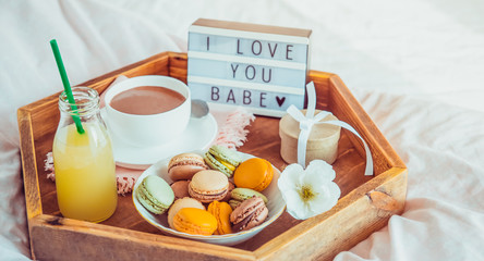 Romantic Breakfast in bed with I love you baby text on lighted box. Cup of coffee, juice, macaroons, flower and gift box on wooden tray. Birthday, Valentine's day morning. Wide banner. Copy space.