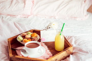 Breakfast in bed with i love you text on a note. Cup of coffee or cocoa, juice, macaroons, rose flower on wooden tray. Romantic breakfast in bed. Birthday, Valentine's day morning. Copy space.