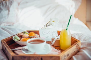 Breakfast in bed with i love you text on a note. Cup of coffee or cocoa, juice, macaroons, rose flower on wooden tray. Romantic breakfast in bed. Birthday, Valentine's day morning. Copy space.
