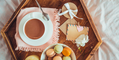 Breakfast in bed with empty blank card. Cup of coffee, juice, macaroons, flower and giftbox on wooden tray. Romantic breakfast in bed. Birthday, Valentine's day morning. Top view. Wide. Copy space.