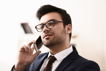 Handsome young businessman talking by mobile phone in office