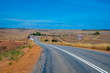 Australian bush road leading through dry landscape and farmland with speed limit 110 kph