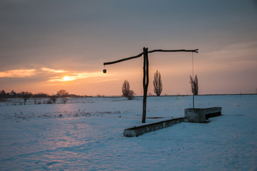 Traditional water well (well sweep or shadoof) during the winter in Serbia with a beautifull sunset