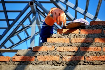 Sunlight and shadow on surface of bricklayer's hand in rubber glove using trowel to build brick...