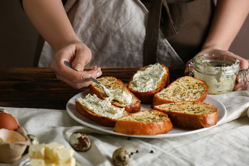 Woman spreading tasty garlic bread with cheese in kitchen