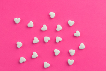 White heart shaped pills on pink background.