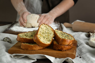 Obraz na płótnie Canvas Tasty cut garlic bread on table and woman kneading dough in kitchen