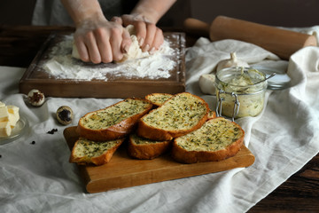 Tasty cut garlic bread on table and woman kneading dough in kitchen