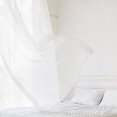 Closeup of white waving curtain on window in white bedroom