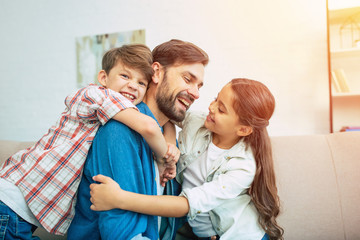 Handsome father is playing and have a fun with his little son and daughter at home on the couch....