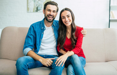 Beautiful young happy couple are sitting on the couch at home and looking on camera